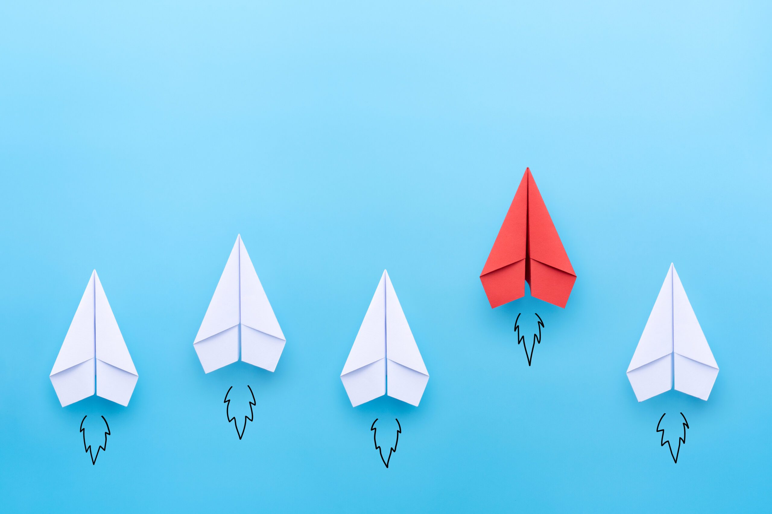 Red paper plane leading among a white planes on blue background